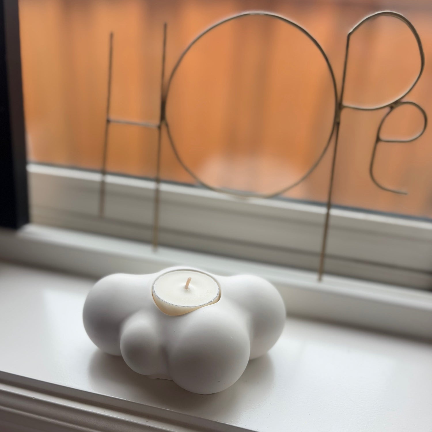 Minimalist cloud-shaped candle holder with a lit tealight, placed on a windowsill.