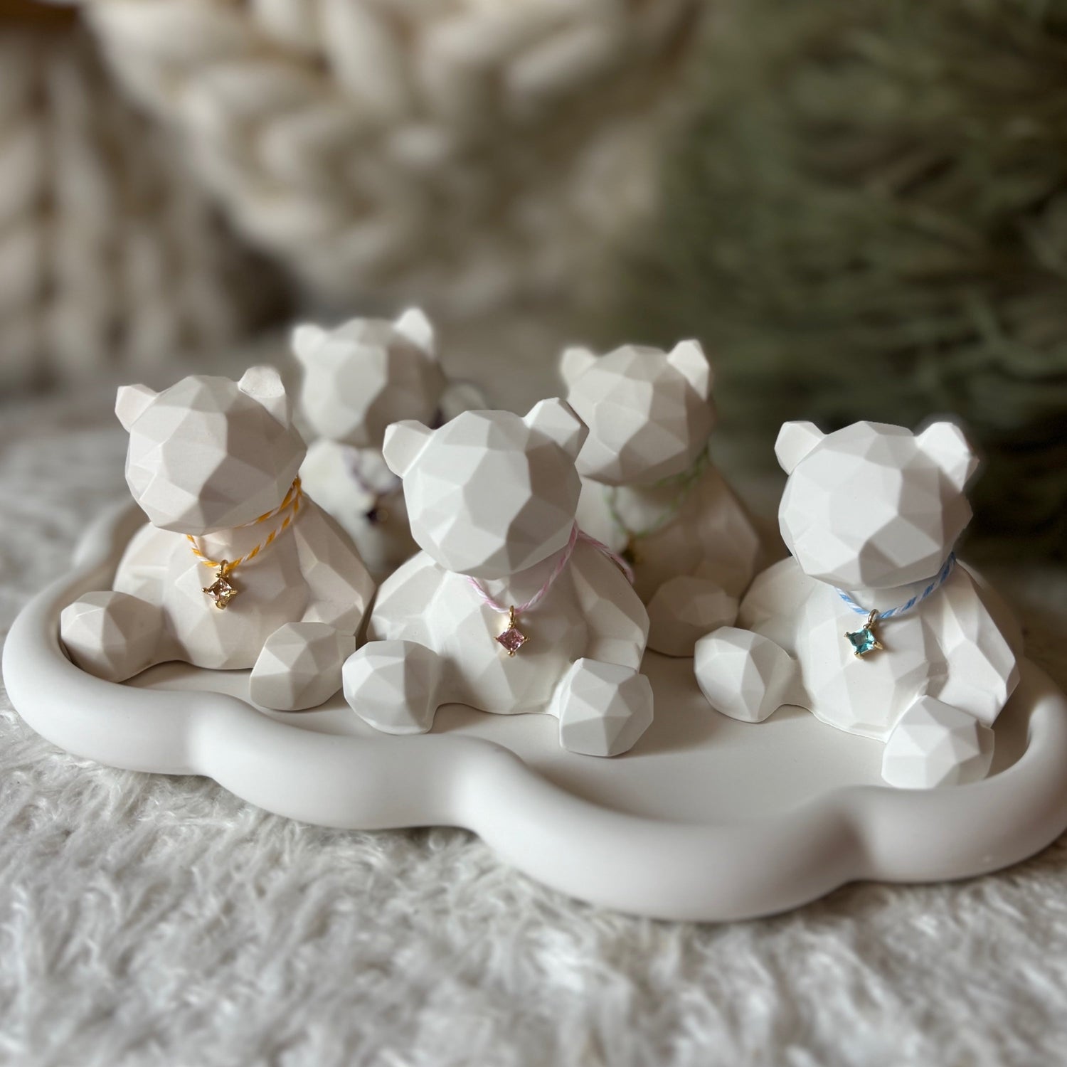 Five faceted white bear figurines on a cloud-shaped tray, each wearing a different ribbon and charm.